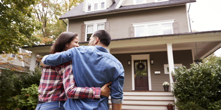 A couple embracing in front of their home.
