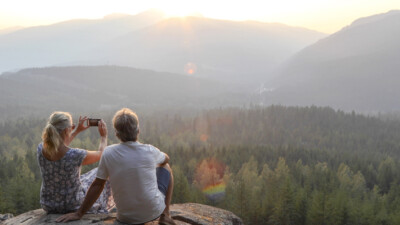 A man and a woman capturing a photograph of a scenic overlook.