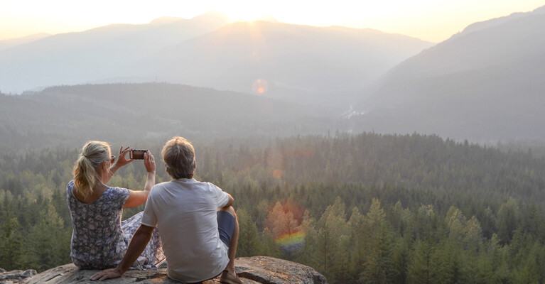 A man and a woman capturing a photograph of a scenic overlook.