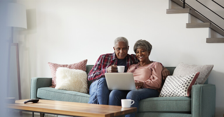 A man and a woman sitting on the couch, looking at a laptop.