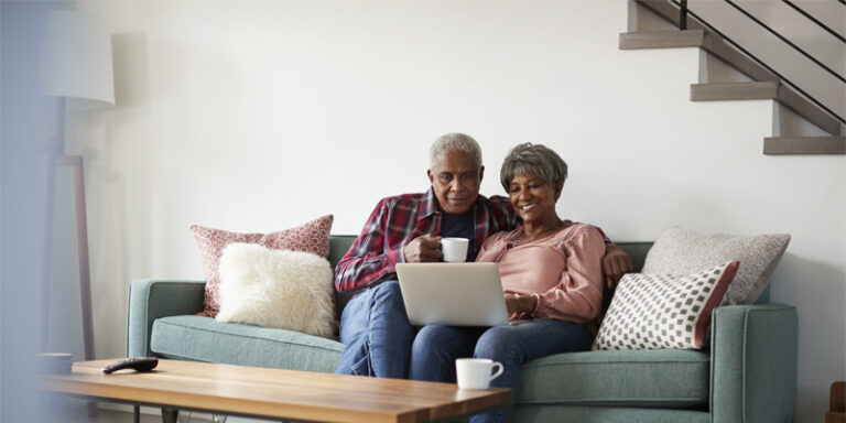 A man and a woman sitting on the couch, looking at a laptop.