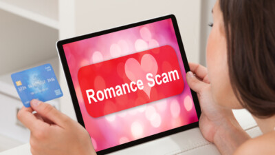 A person looking at their credit card and a tablet that says, “romance scam.”