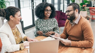 Two women and a man talking around a laptop.