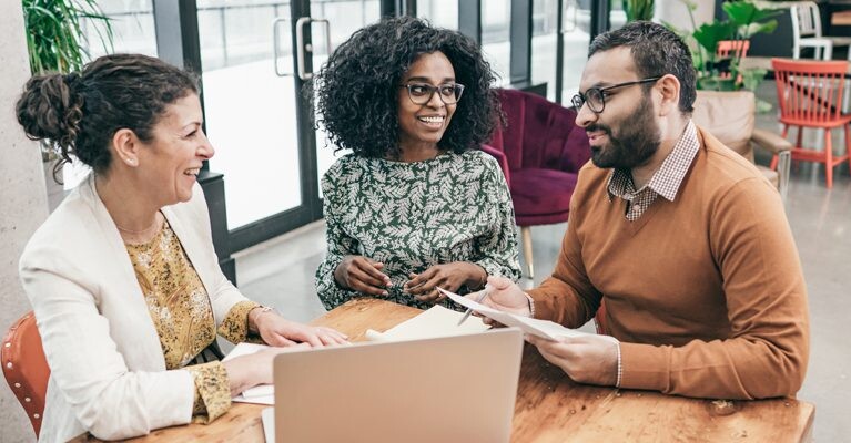 Two women and a man talking around a laptop.