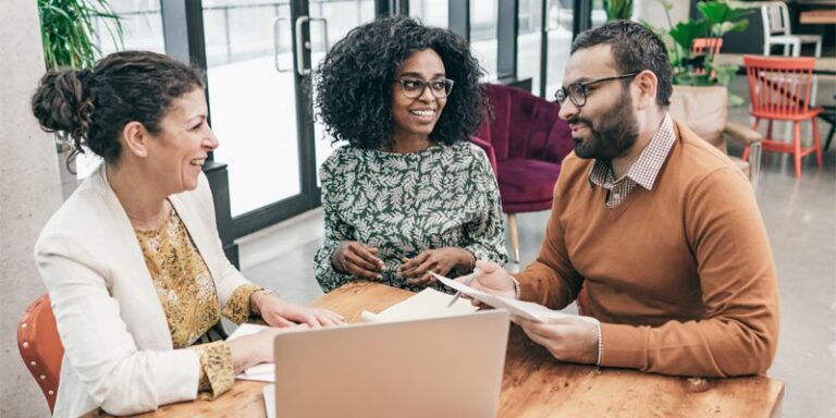 Two women and a man talking around a laptop.