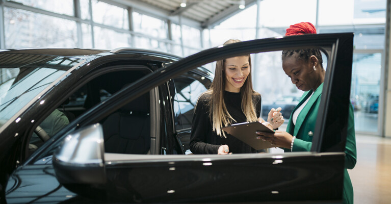 A customer and a car salesman signing paperwork for a new car.