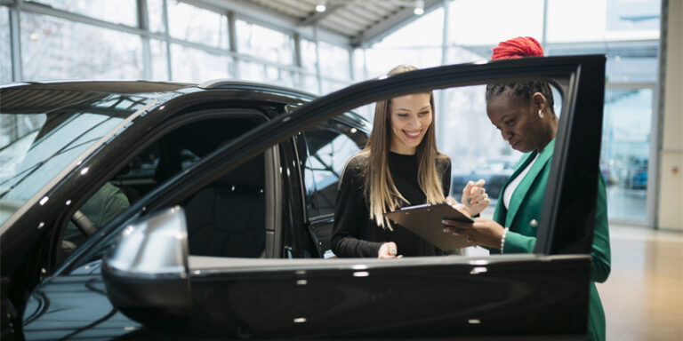 A customer and a car salesman signing paperwork for a new car.