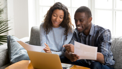 Woman and man using laptop and holding papers.