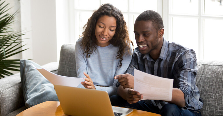 Woman and man using laptop and holding papers.