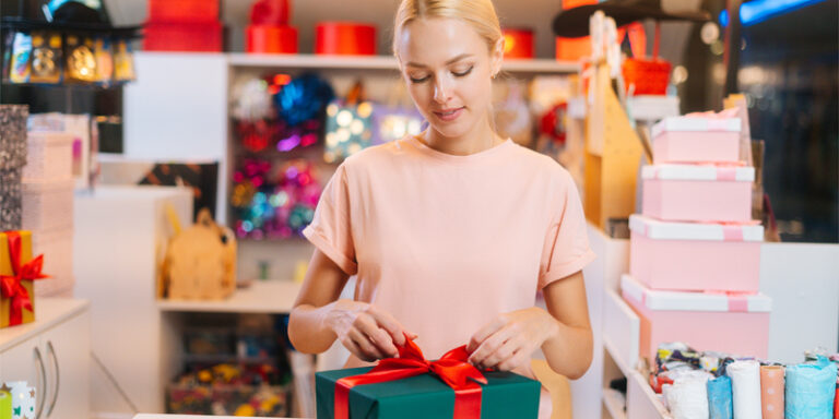 A woman tying a bow on a gift box.