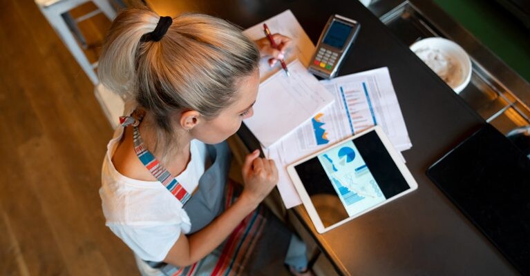 Small business owner doing paperwork in front of a payment terminal.