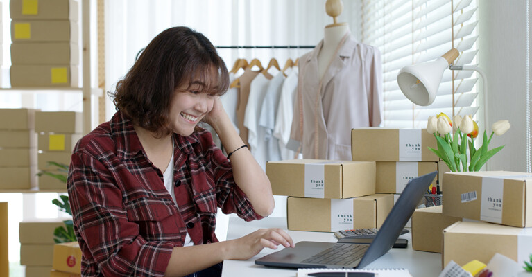 Small business owner packaging orders in front of computer.