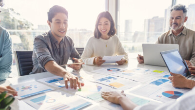 A group of businesspeople sitting around a table, looking at printouts of charts and graphs.