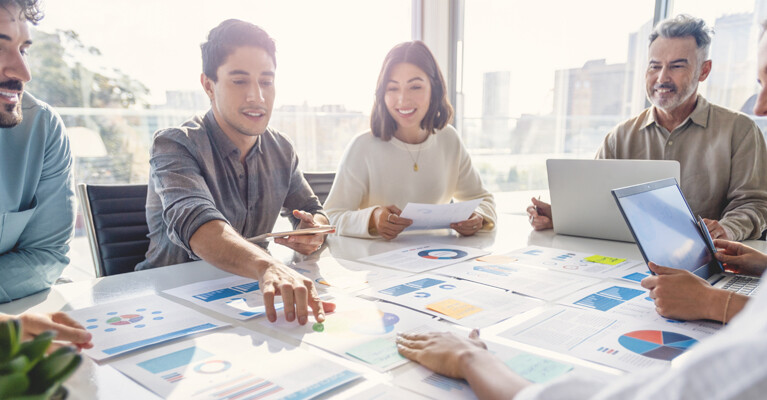 A group of businesspeople sitting around a table, looking at printouts of charts and graphs.