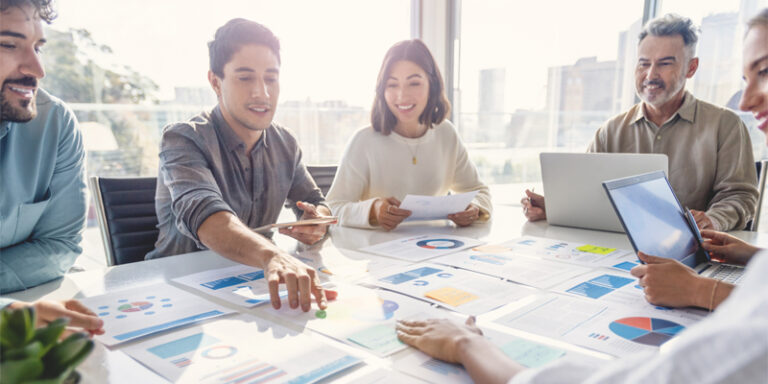 A group of businesspeople sitting around a table, looking at printouts of charts and graphs.