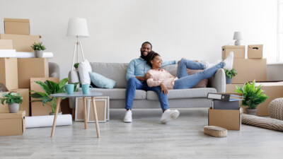 A couple relaxing on the couch in their new home, amidst unpacked boxes.