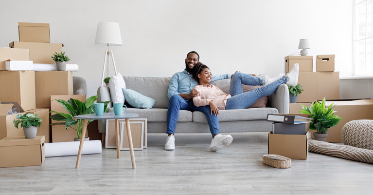 A couple relaxing on the couch in their new home, amidst unpacked boxes.