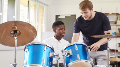 A teacher showing a student how to play a drum kit.