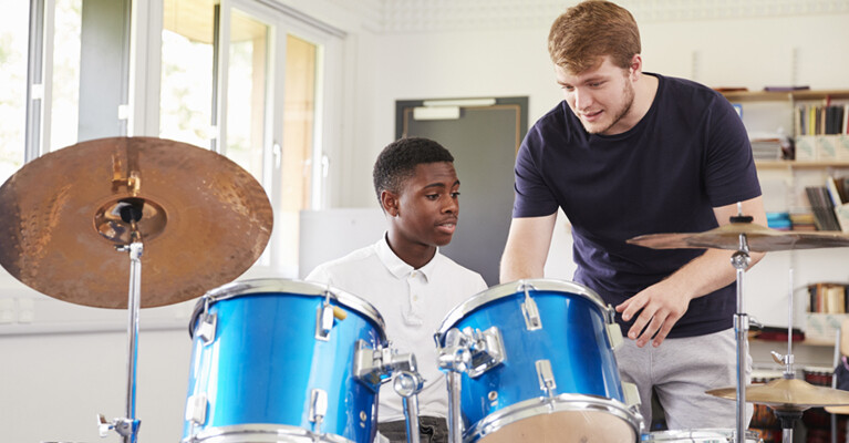 A teacher showing a student how to play a drum kit.