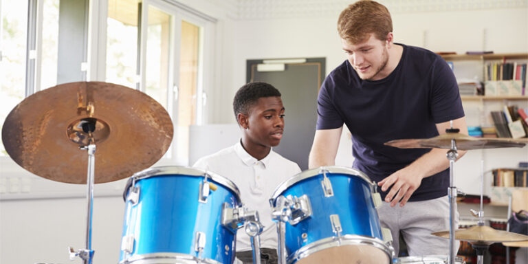 A teacher showing a student how to play a drum kit.
