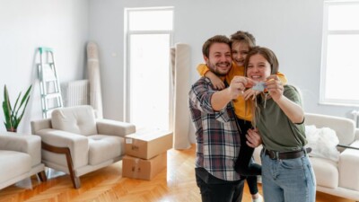 Man, woman, and child, holding house keys and smiling in front of moving boxes.