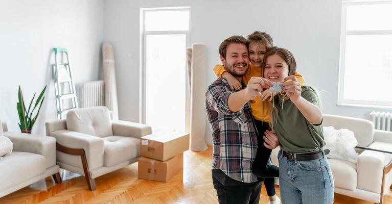 Man, woman, and child, holding house keys and smiling in front of moving boxes.