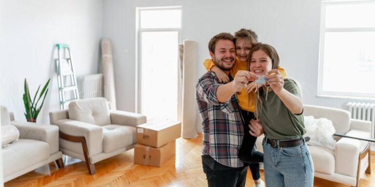 Man, woman, and child, holding house keys and smiling in front of moving boxes.