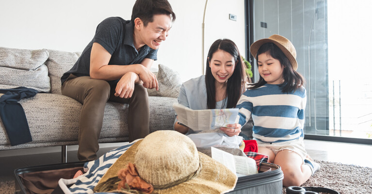 Man, woman, and child looking at map and packing suitcase.