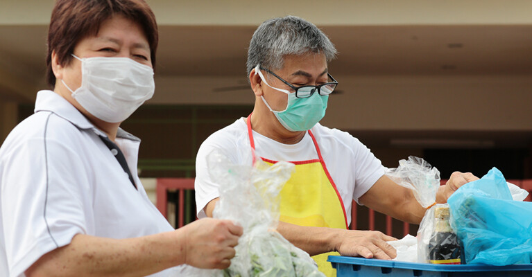 Two masked volunteers packing food supplies.