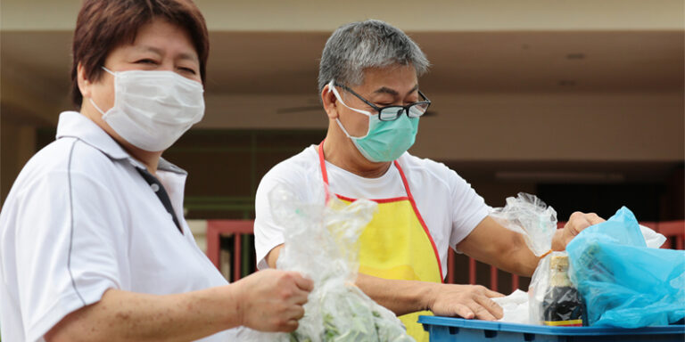 Two masked volunteers packing food supplies.