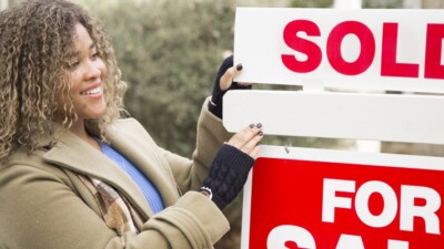 Woman in front of "Sold" sign.