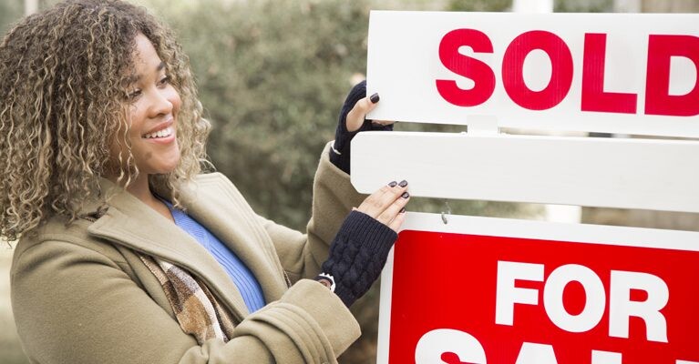 Woman in front of "Sold" sign.