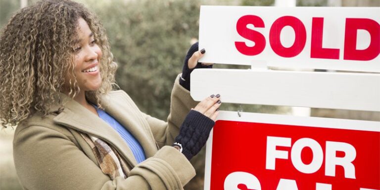 Woman in front of "Sold" sign.