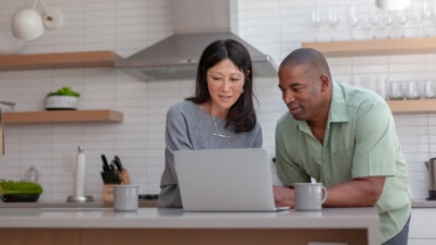 Woman and man looking at a laptop, standing at a kitchen island.