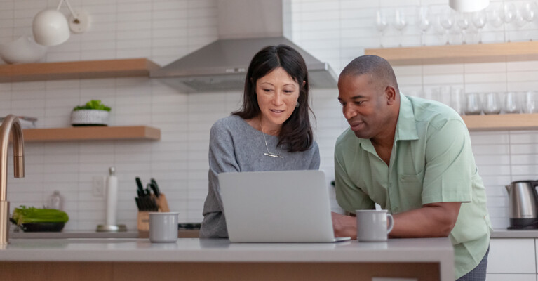 Woman and man looking at a laptop, standing at a kitchen island.