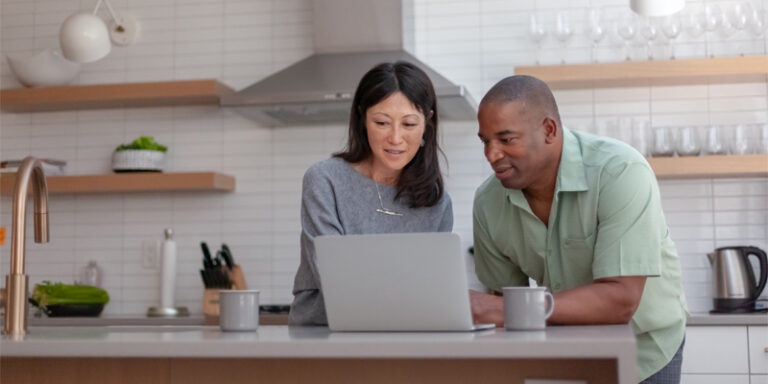 Woman and man looking at a laptop, standing at a kitchen island.