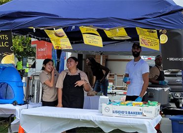 People laughing under a covered food stand.