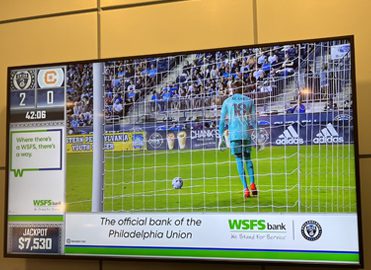 The Philadelphia Union match on a TV at Subaru Park with an ad that reads “WSFS Bank, the official bank of the Philadelphia Union.”