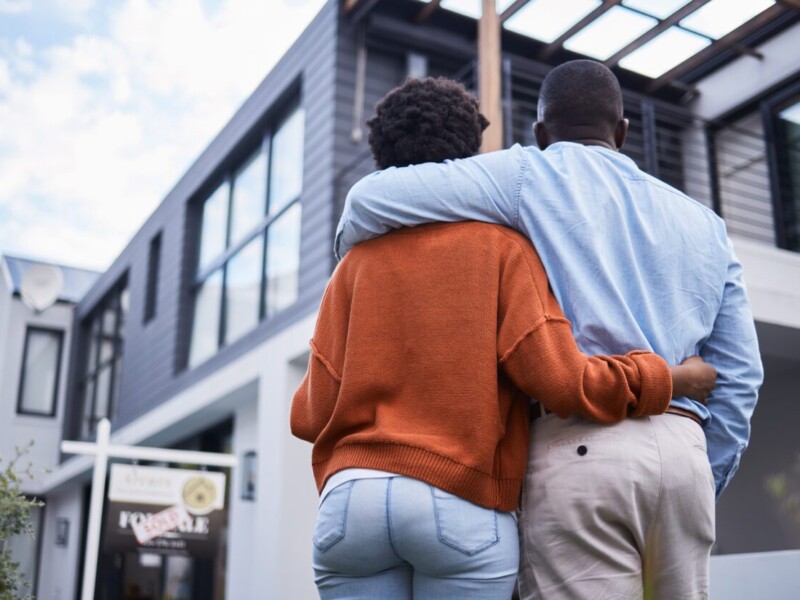 Woman and man embracing in front of new home.