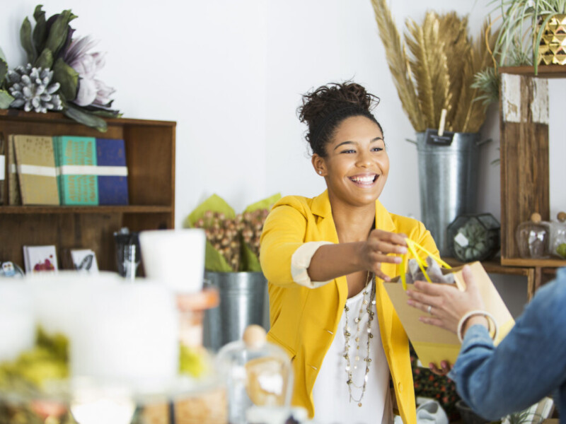 Woman handing purchase over counter to customer.