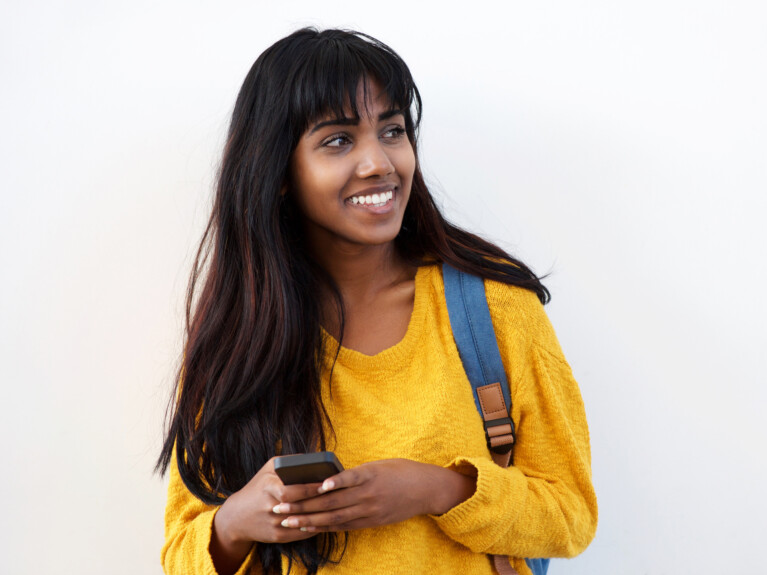 Young woman in yellow sweater, with a backpack and a cell phone.