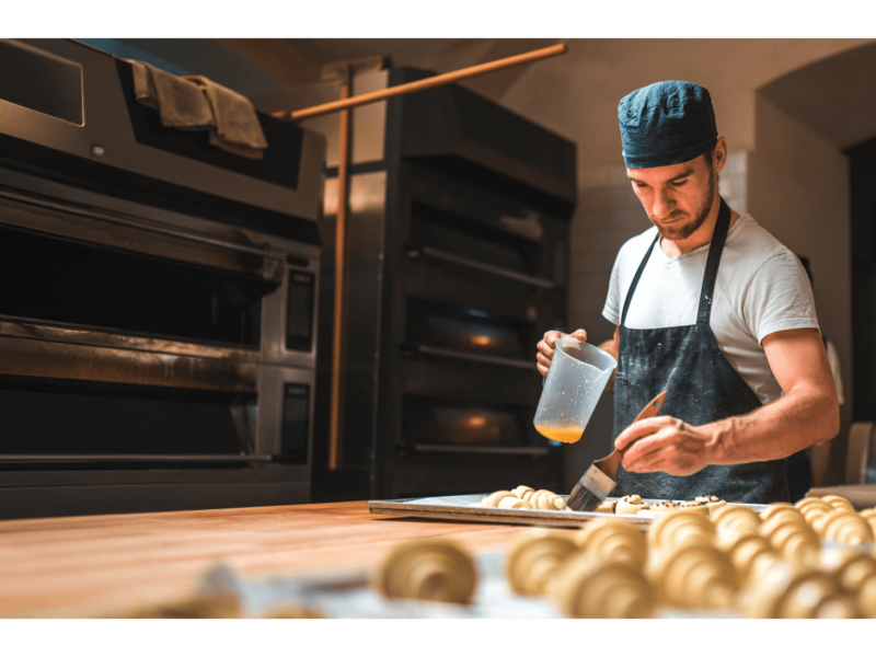 A male baker buttering pastries.