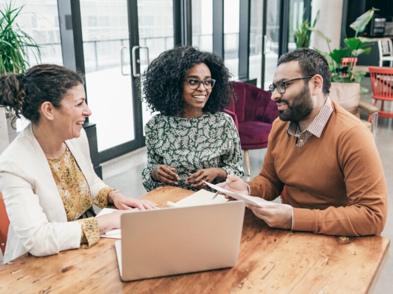 Three businesspeople discussing around a laptop.