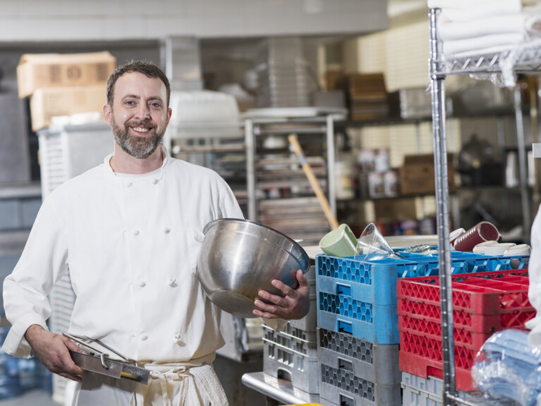 A chef holding a mandolin slicer and a mixing bowl.