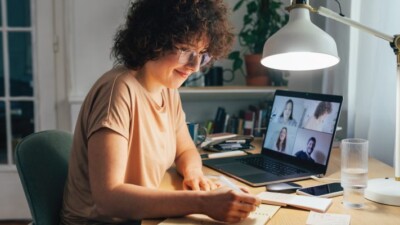 A woman writing in a notebook while on a video call with other people.