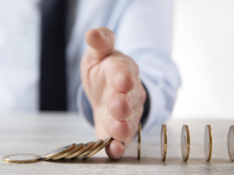 A hand stopping a stack of coins from falling over.