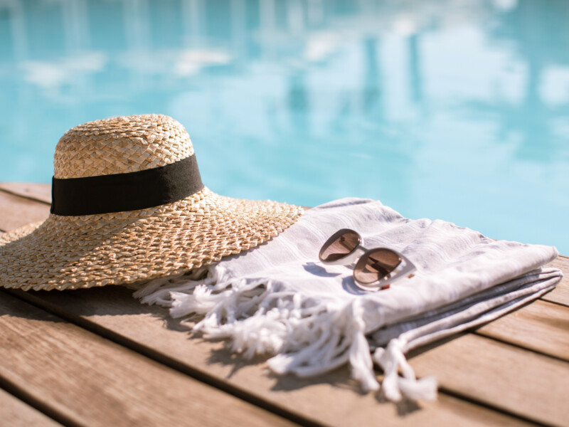 Sunglasses and straw hat on the wooden floor at the pool.
