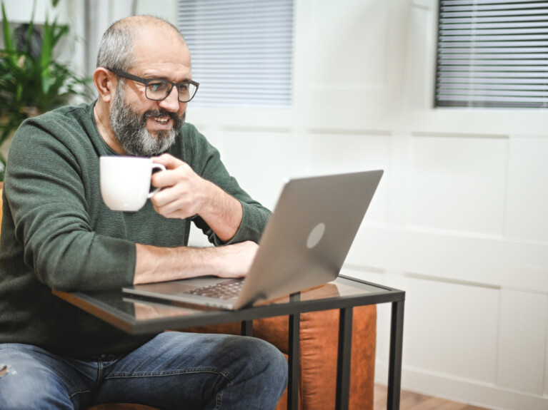 A man holding a mug and working at his laptop.