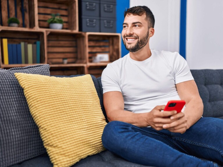 Man sitting on couch, holding cell phone.
