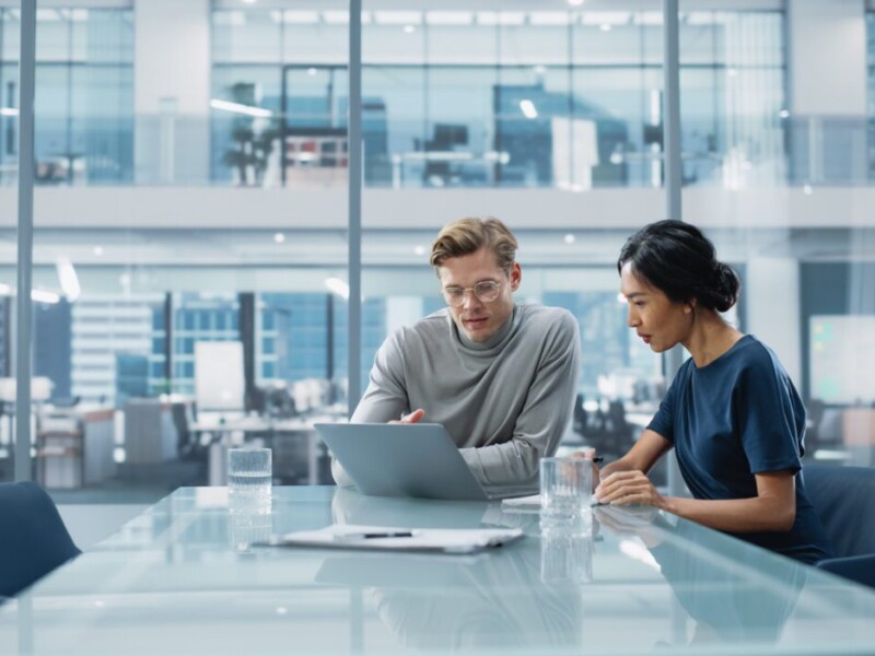 Man and woman looking at a laptop while sitting in a meeting room.